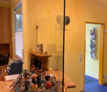 Gebogenes Einscheibensicherheitsglas 8 mm an die Biegung des Empfang-Tresens angepasst und mit Glasklemmhaltern befestigt.